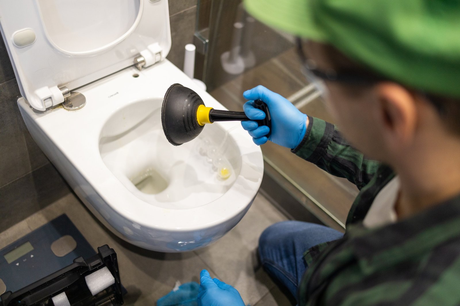 Cleaning toilet stuck with suction cup. Hands in gloves holding ventuz in toilet.