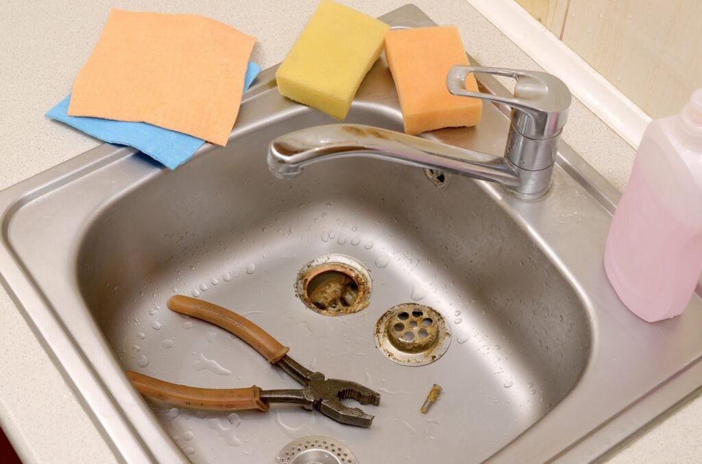 Pliers inside the silvery sink with a disassembled protective filter. Kitchen sink repair process